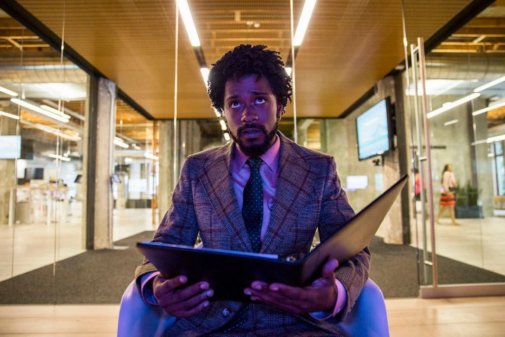 Photo de Lakeith Stanfield assis devant un immeuble, le visage illuminé par une lueur violette dans le film Sorry to Bother You.