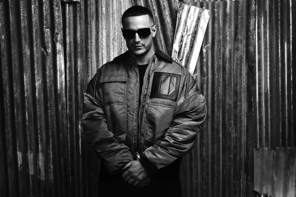 En concert à Paris le 10 mai 2025, l'artiste Dj Snake prend la pose dos à un mur en fer, dans un cliché en noir et blanc.
