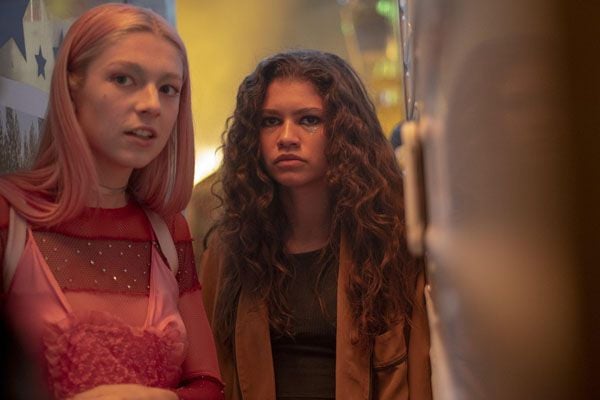 Hunter Schafer en top rose et Zendaya en veste en daim marron dans la série Euphoria.