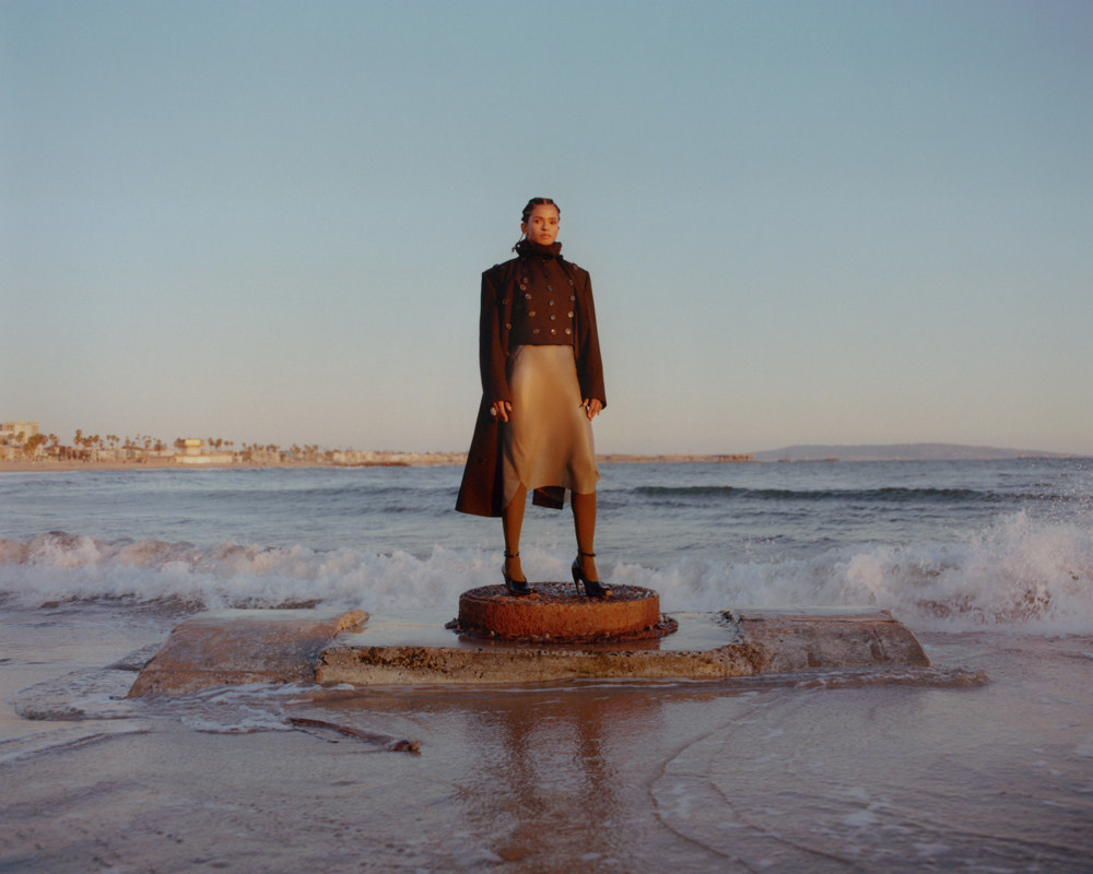 Portrait de Ramla Ali par Elliot James Kennedy. Manteau et veste en laine, jupe en latex et escarpins, Alaïa. Bague “Panthère” en or blanc, onyx, grenats tsavorites et diamants, Cartier.