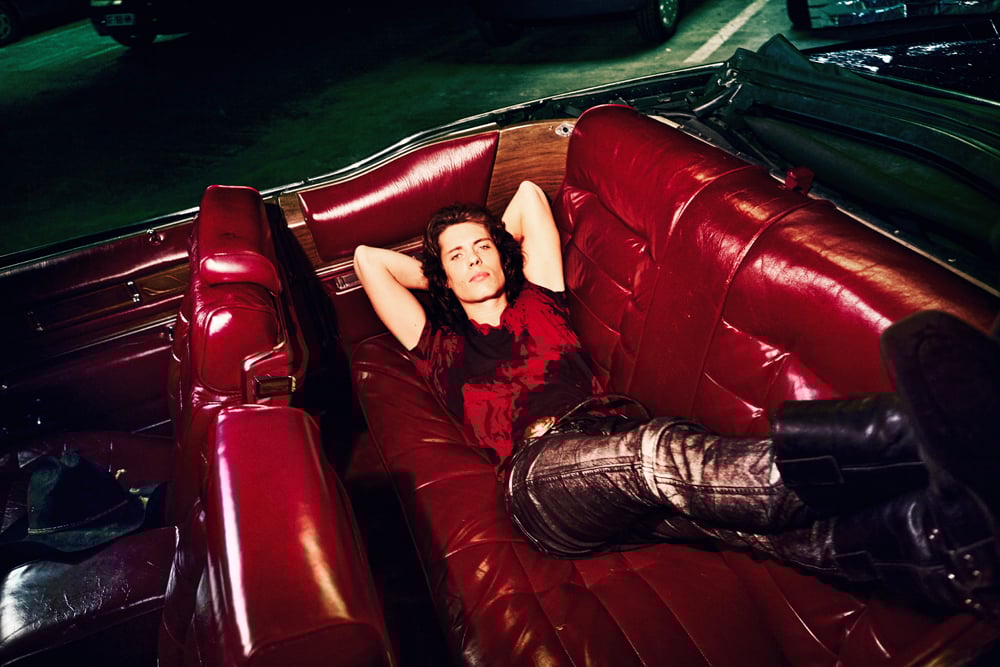 L'artiste Asphalt prend la pose allongé sur un canapé rouge, sélectionné dans les chanteurs à suivre selon Numéro © Elle Von Unwerth.