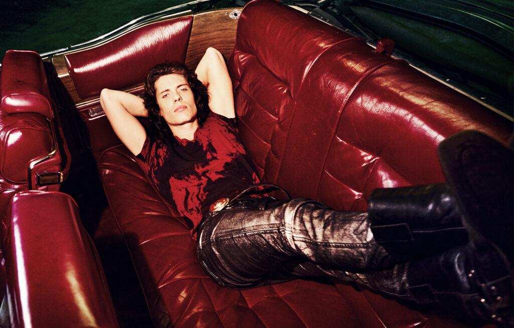 Artist Asphalt strikes the pose, lying down on a red sofa. Selected by Numéro among the singers to watch closely © Elle Von Unwerth.
