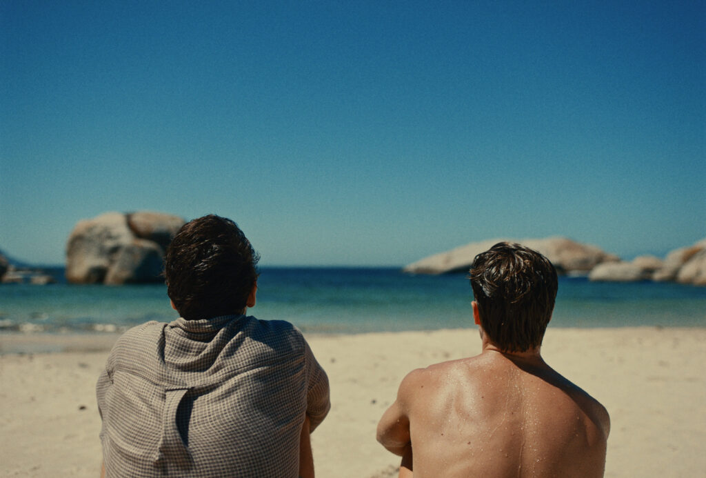 Deux hommes font face à l'océan sur une plage ensoleillée dans le film Moffie (2019) d'Oliver Hermanus. 