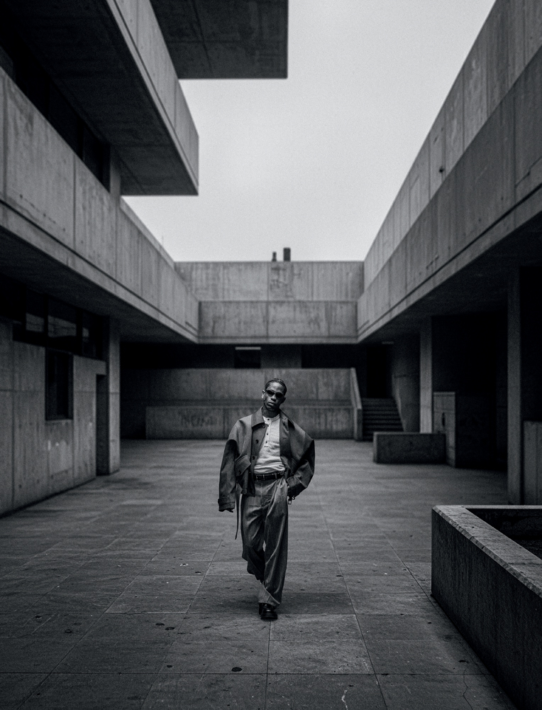 Portrait de Travis Scott en noir et blanc en milieu urbain, avec des lunettes de soleil.