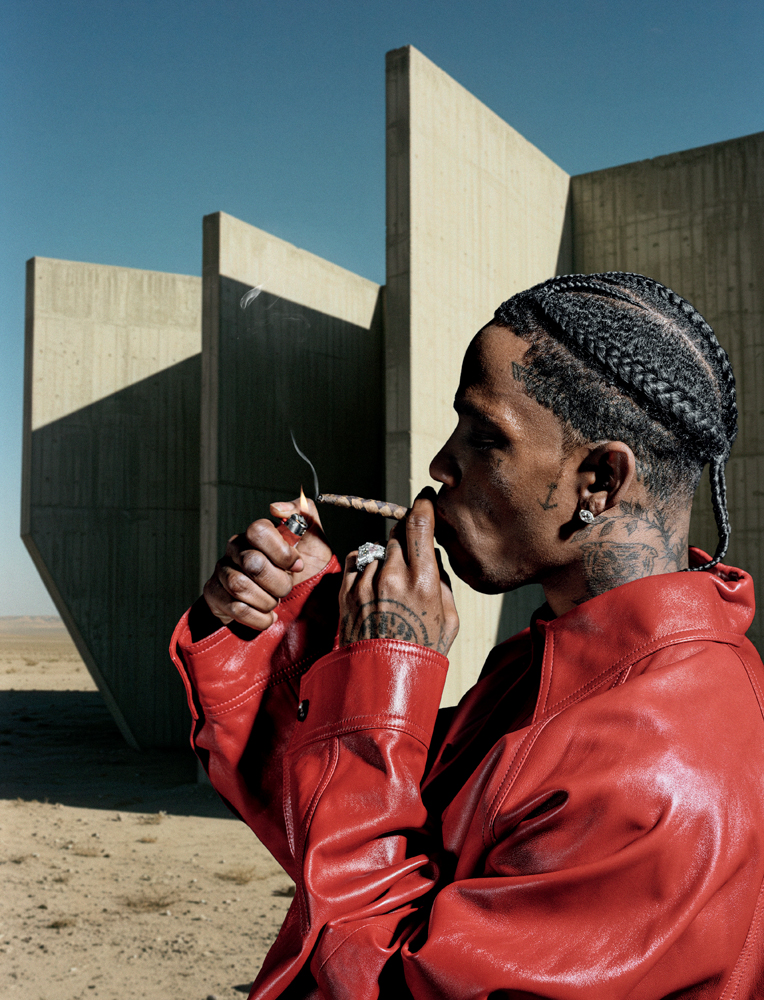 Portrait de côté de Travis Scott en blouson en cuir rouge, fumant un cigare monogrammé.