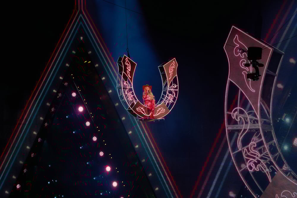 Photo de Beyoncé suspendue dans les airs assise sur un grand fer à cheval dans un look rouge Moschino et Swarovski.