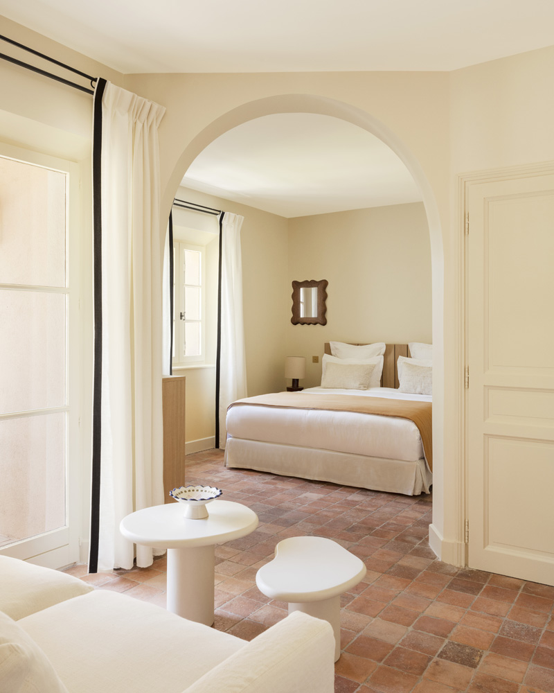 Vue d'une chambre avec petit salon, mobilier blanc apaisant et tomettes au sol.