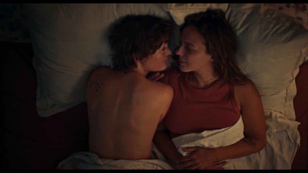 Vicky Krieps et Monia Chokri allongées dans un lit dans le film Love Me Tender (2025).