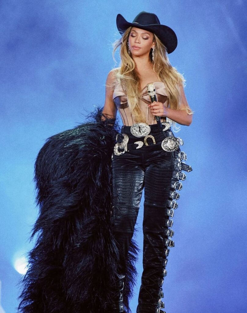 Photo de la chanteuse Beyoncé en pantalon à sangles en cuir noir custom Schiaparelli Haute Couture pendant un concert de sa tournée Cowboy Carter Tour.