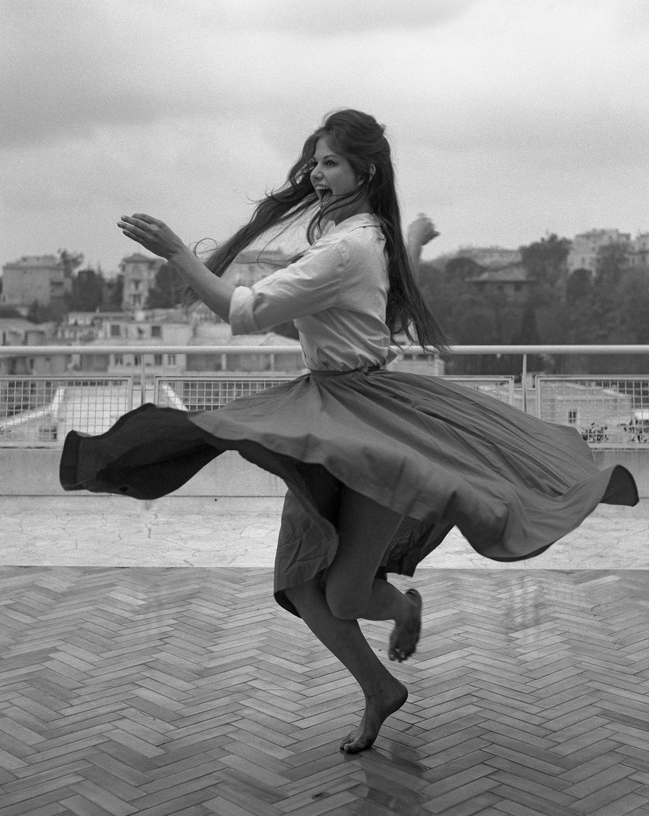 L’actrice italienne Claudia Cardinale, vêtue d’une chemise et d’une jupe ample, danse pieds nus sur une terrasse sur les toits de Rome, en 1959.