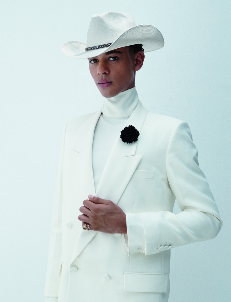 portrait du danseur étoile Guillaume Diop en veste croisée en grain de poudre et sous-pull à col roulé en crêpe de soie Gucci, un chapeau Stetson, fleur Cinabre et bagues Cartier.
