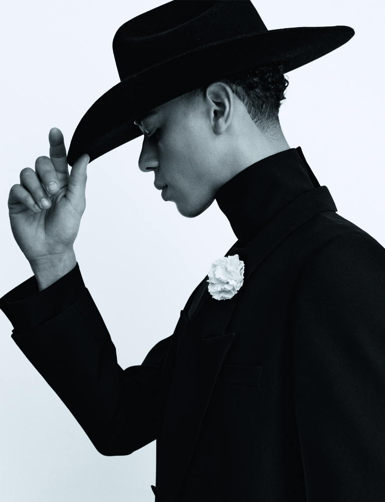 portrait du danseur étoile Guillaume Diop en veste croisée en grain de poudre et sous-pull à col roulé en crêpe de soie Gucci, un chapeau Stetson et une fleur Cinabre.