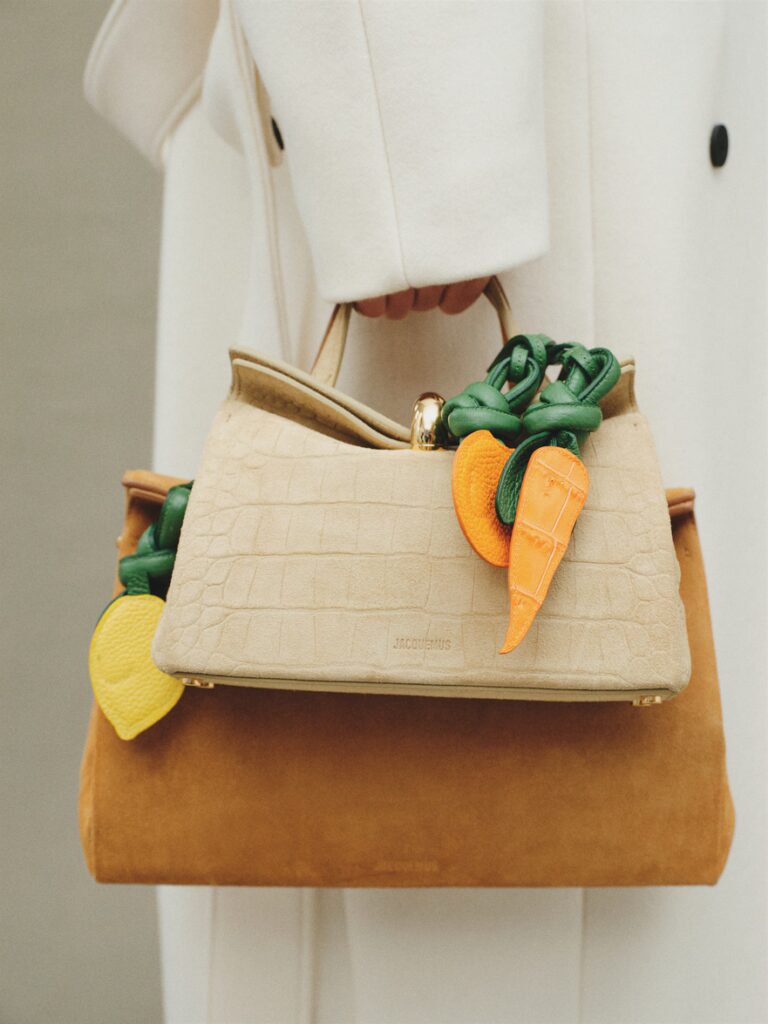 Le sac Valérie de Jacquemus en daim beige et sable, décoré de charms carottes, citron.