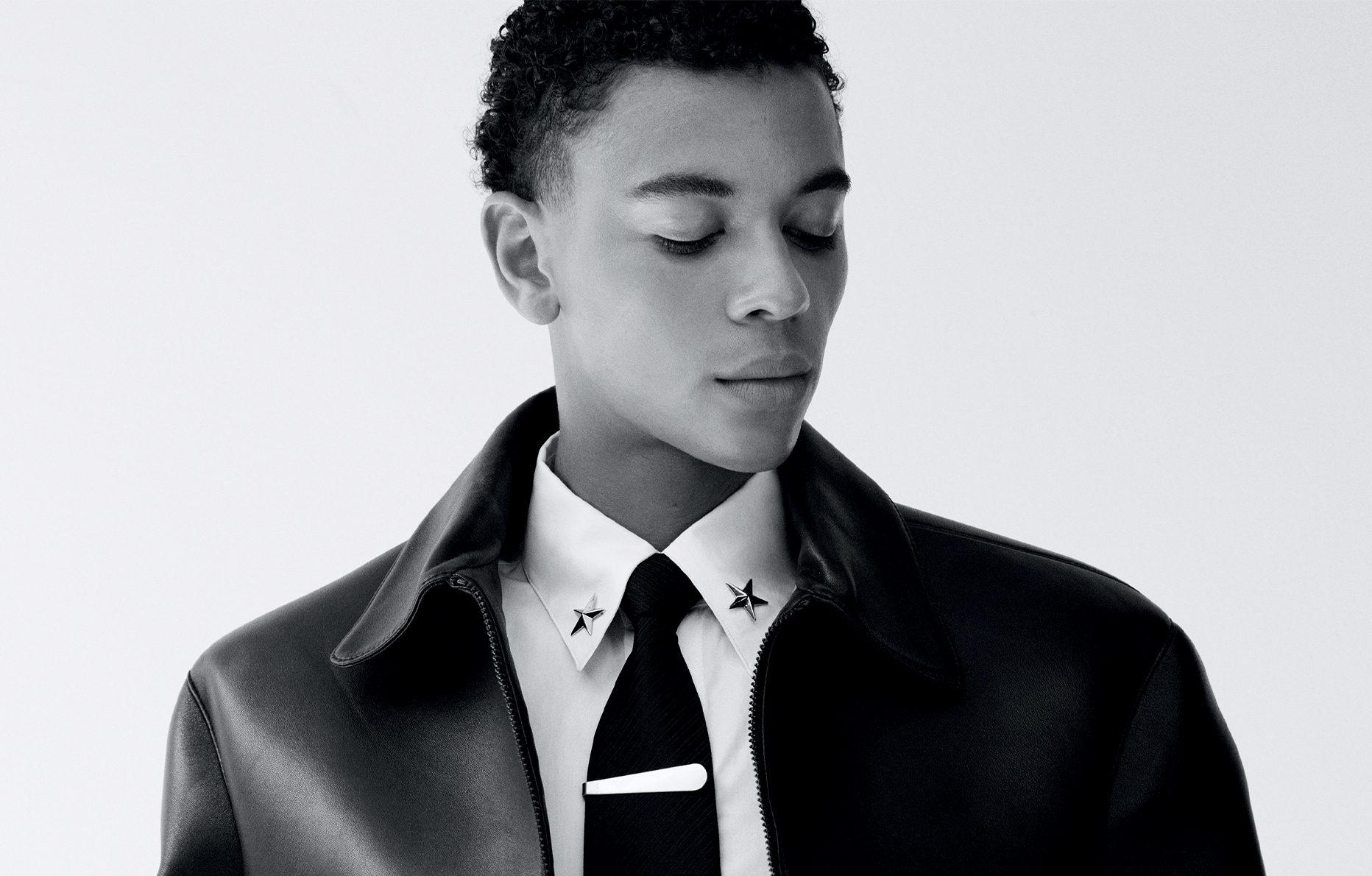 Guillaume Diop porte un blouson zippé en cuir Dior Men, une chemise en popeline de coton et cravate Charvet, un caleçon en popeline de coton Hermès, des bagues Cartier. Une pince à cravate Dary's et des bijoux de col vintage.